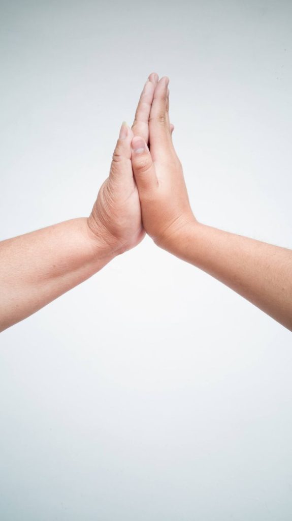 A close-up image of two adult hands high-fiving against a white background in a vertical shot.